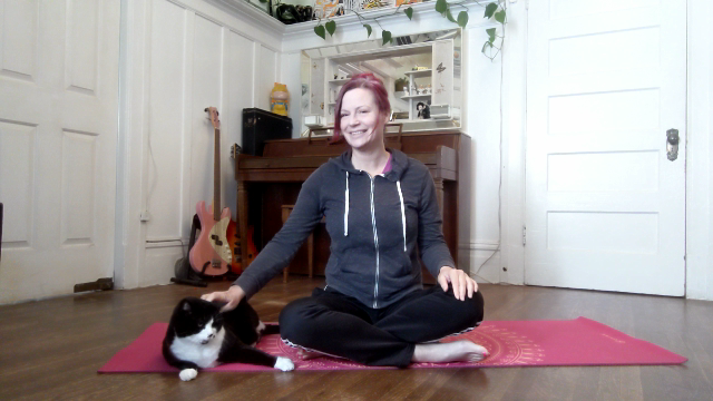 Person sitting on a pink mat with a tuxedo cat sitting next to her.