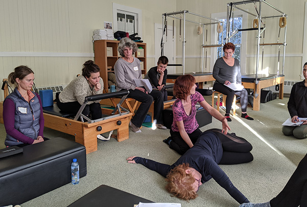 Group of people sitting on equipment at a Pilates studio.