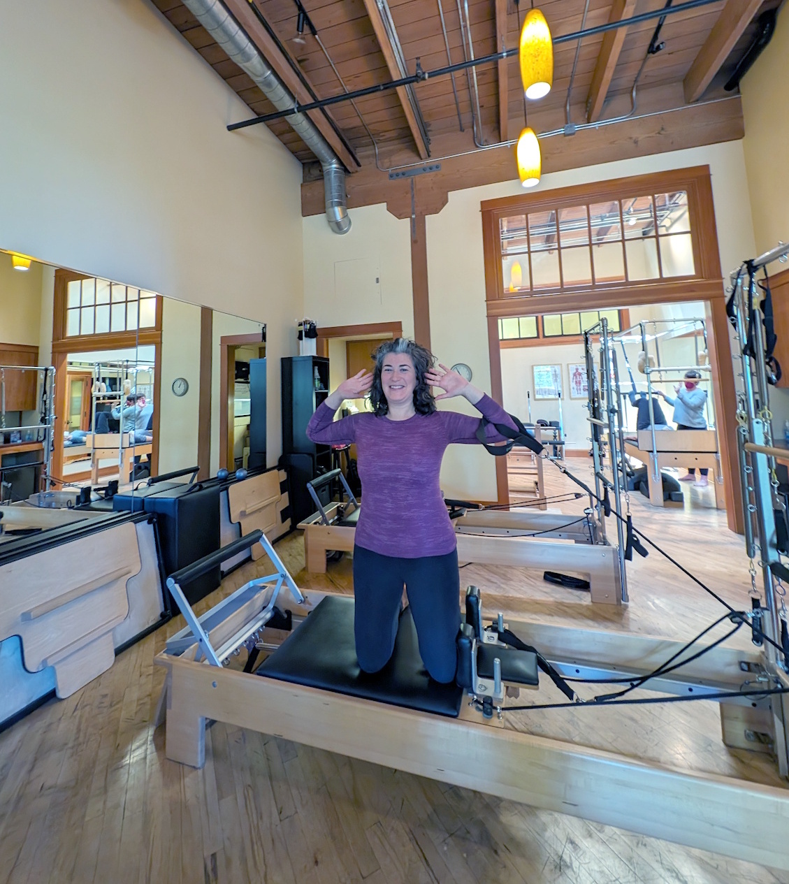 A person in a side kneeling position on the reformer Pilates equipment.