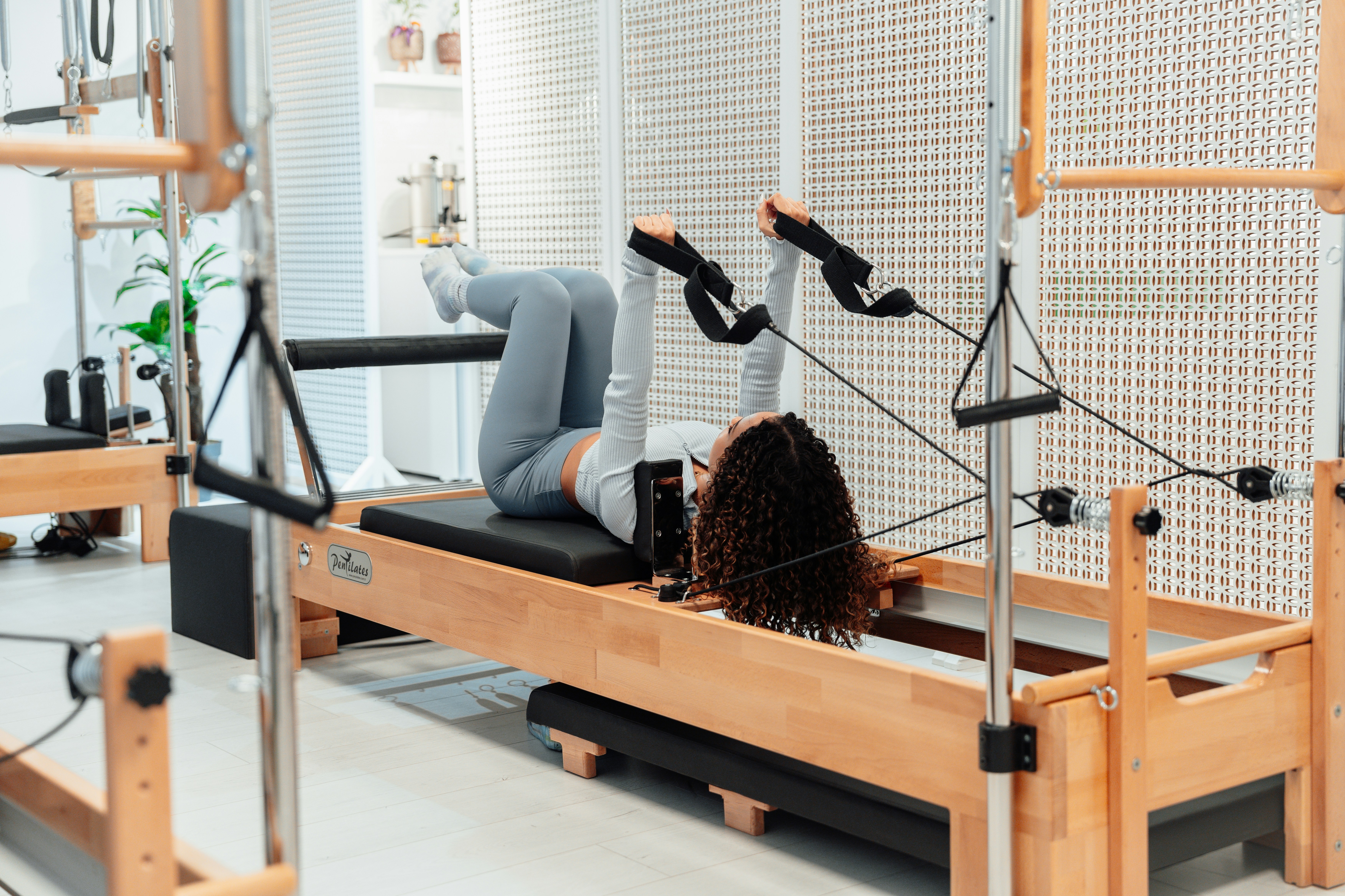 Woman on the Pilates reformer with her hands in the straps.