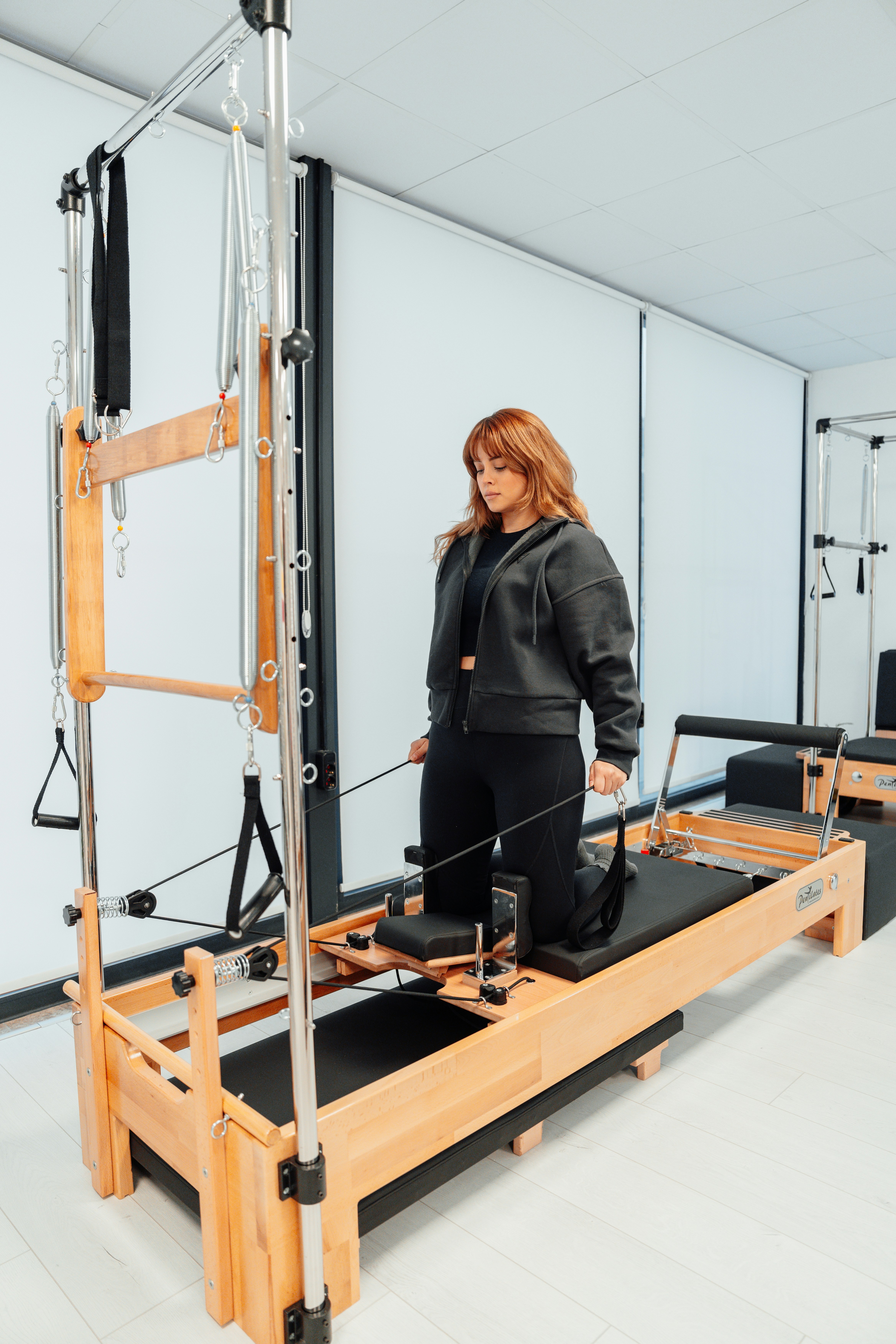 A woman kneeling on the reformer preparing to do the chest expansion exercise.
